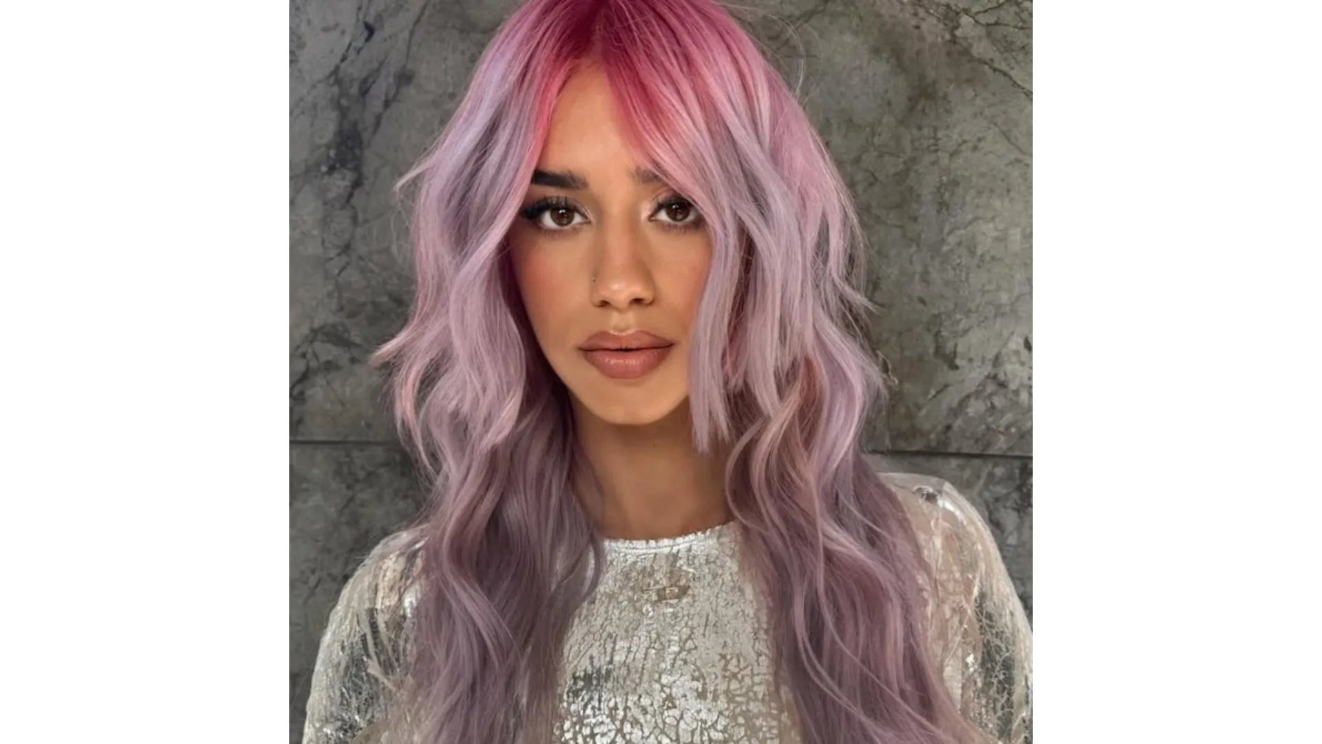 Model with long, wavy hair that’s bright pink at the roots and lilac through the lengths.