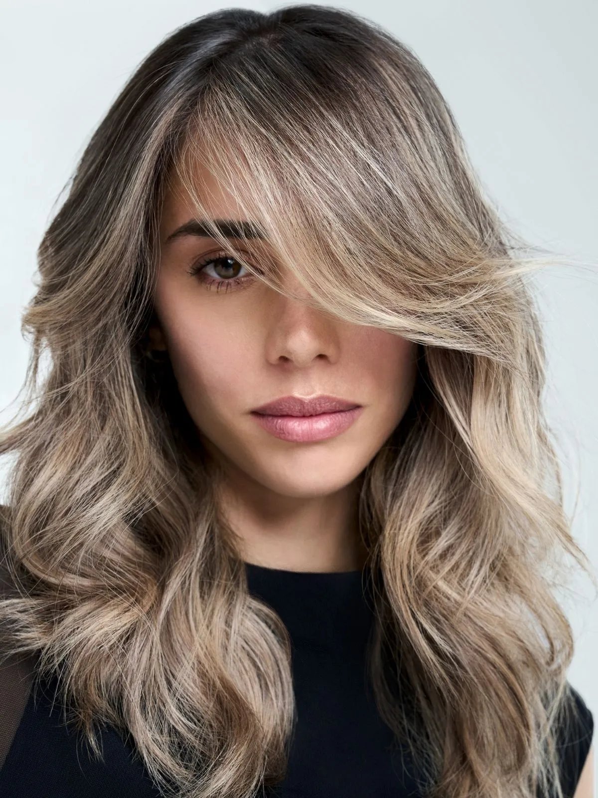 Model with ashy blonde balayage styled in loose, beachy waves.