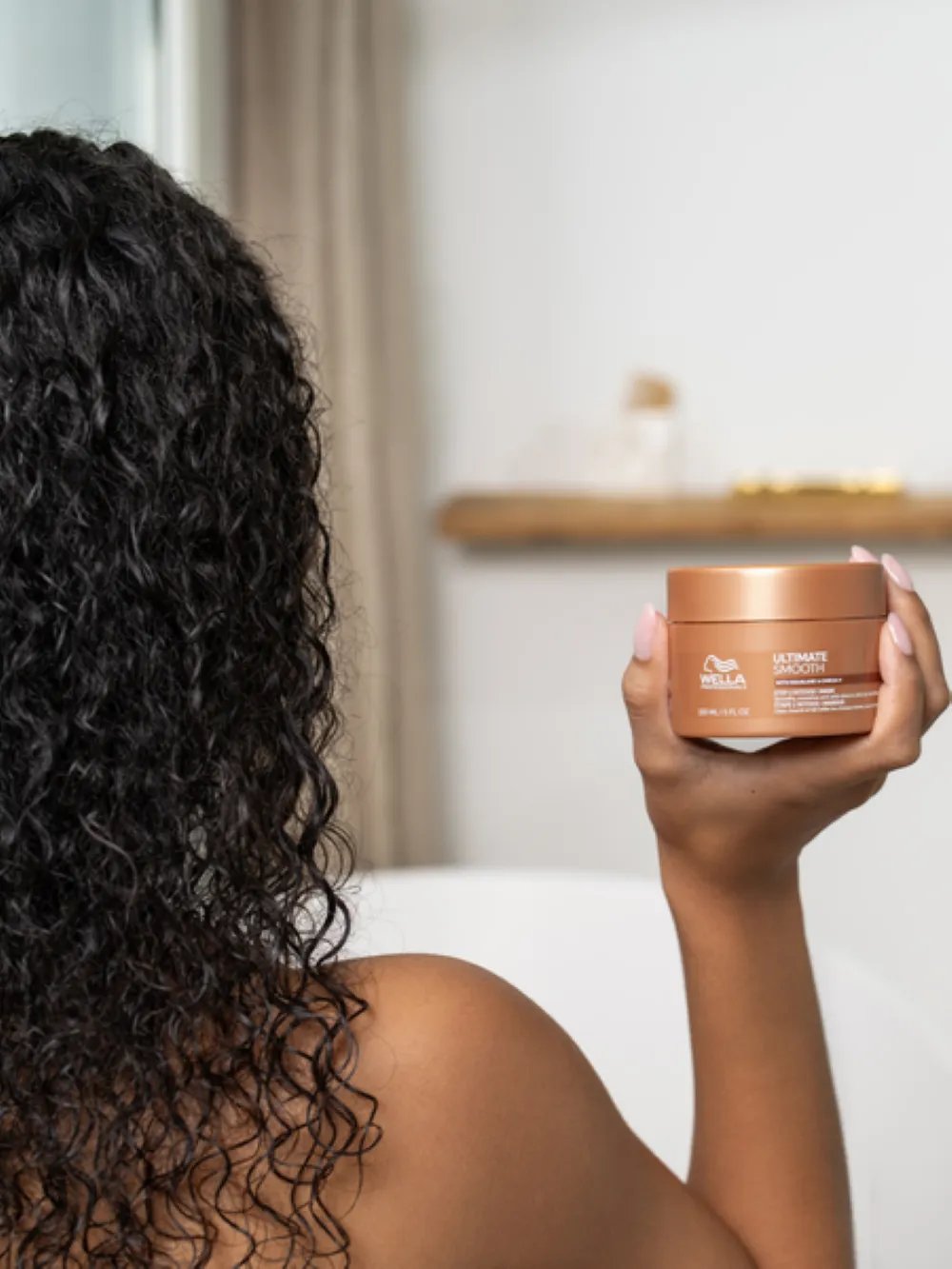 Model with curly hair holding a Wella Professionals hair mask jar.