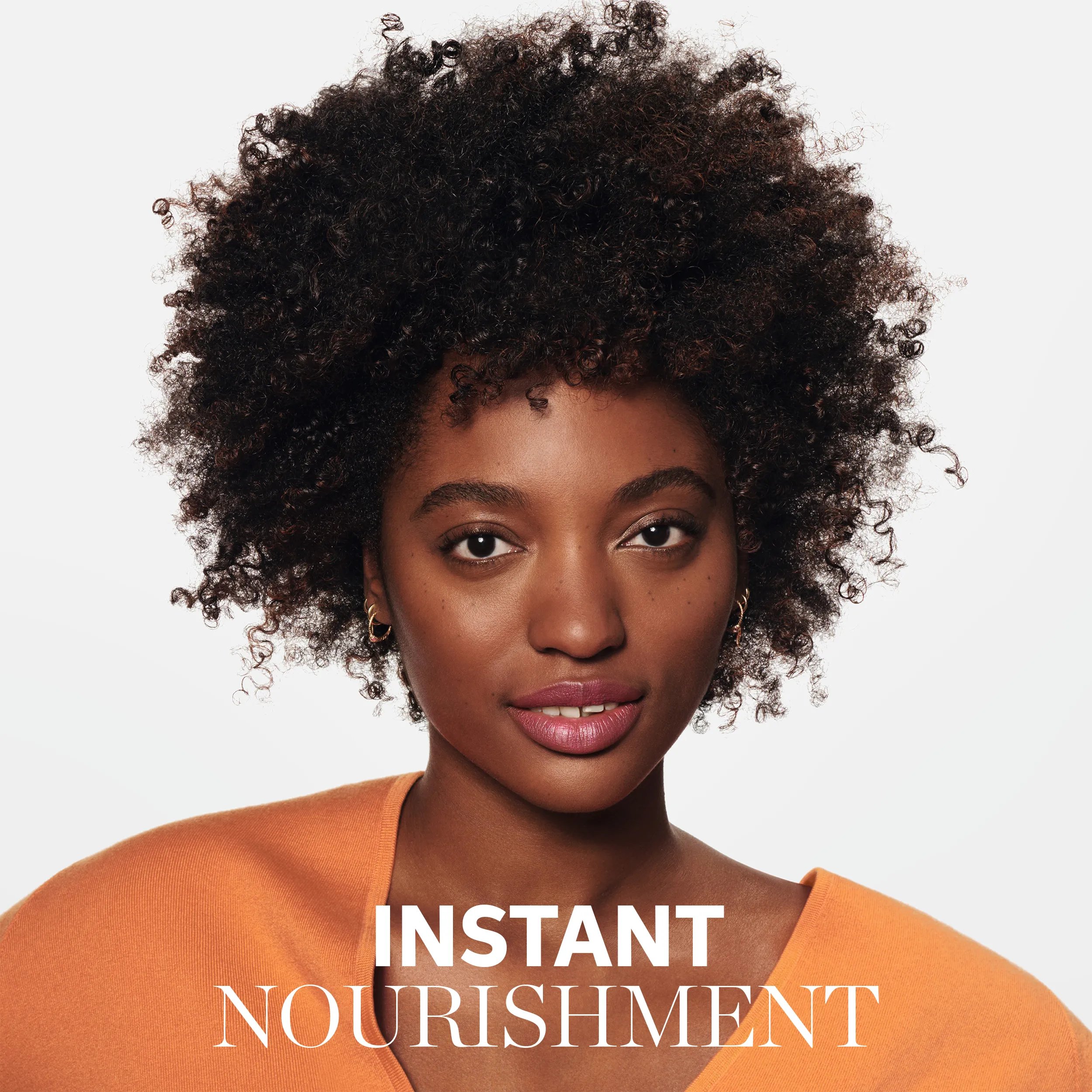 Close-up of a model with curly hair and an orange top, overlaid with the text "Instant Nourishment."
