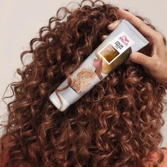 Model with caramel brown, curly hair holds up Color Fresh Mask in Caramel Glaze. 
