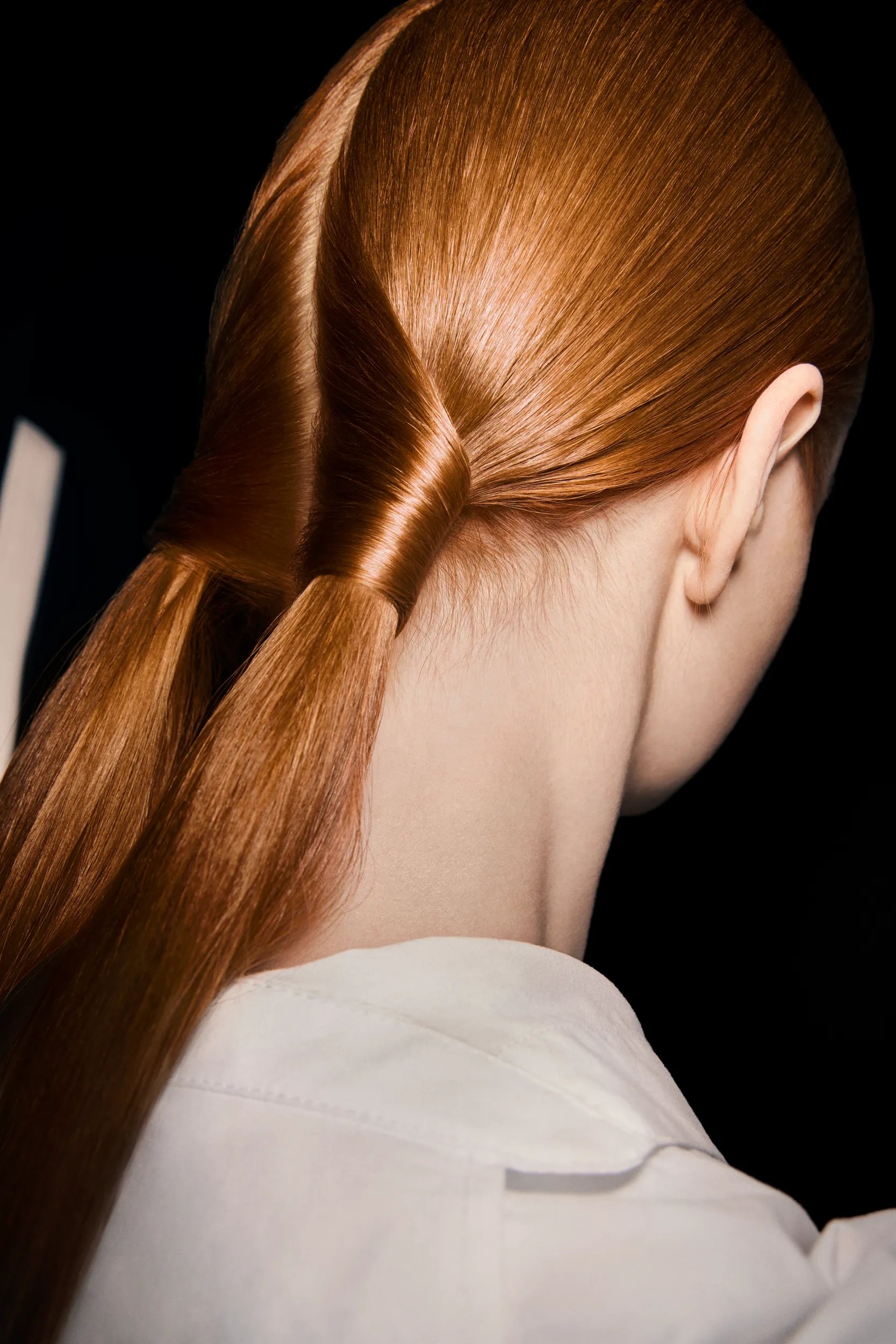 Image montrant le détail de la coiffure d'un mannequin. Les cheveux roux du mannequin sont tordus selon un motif complexe. 