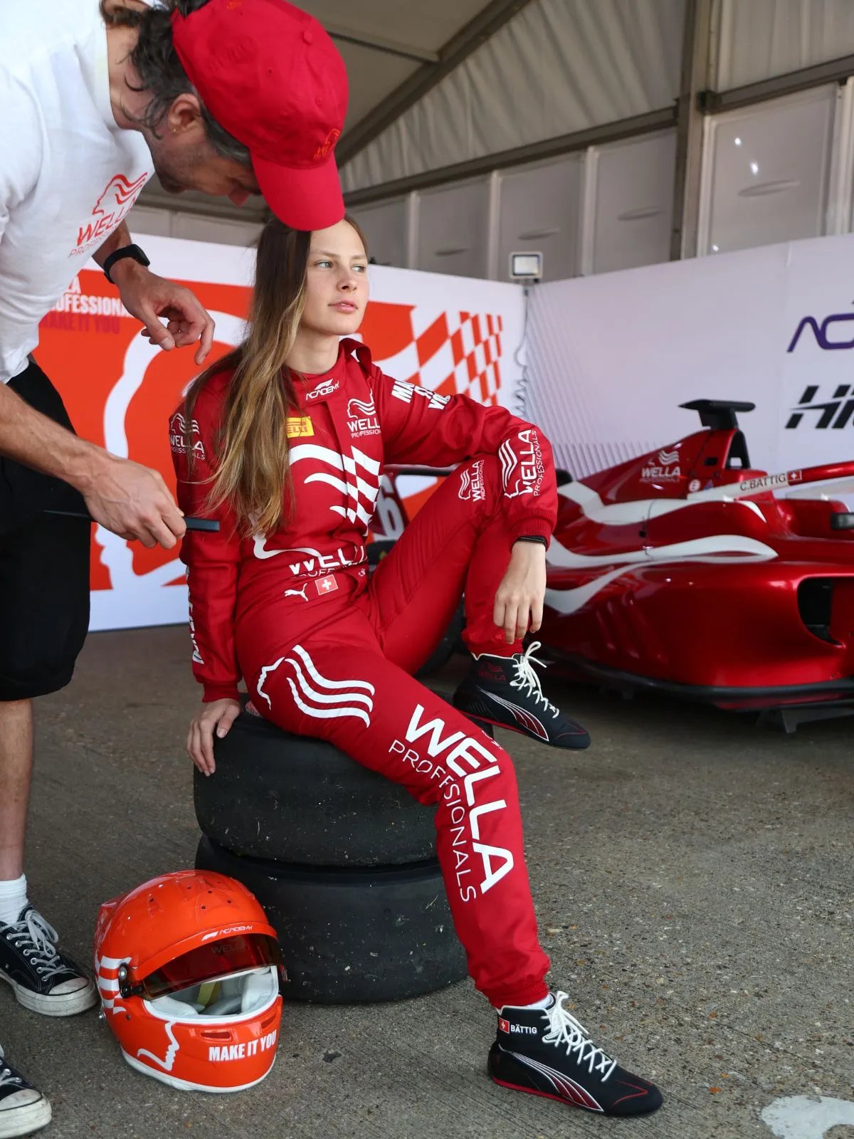Chiara Bättig hair is prepped for photos next to her Wella red racecar.
