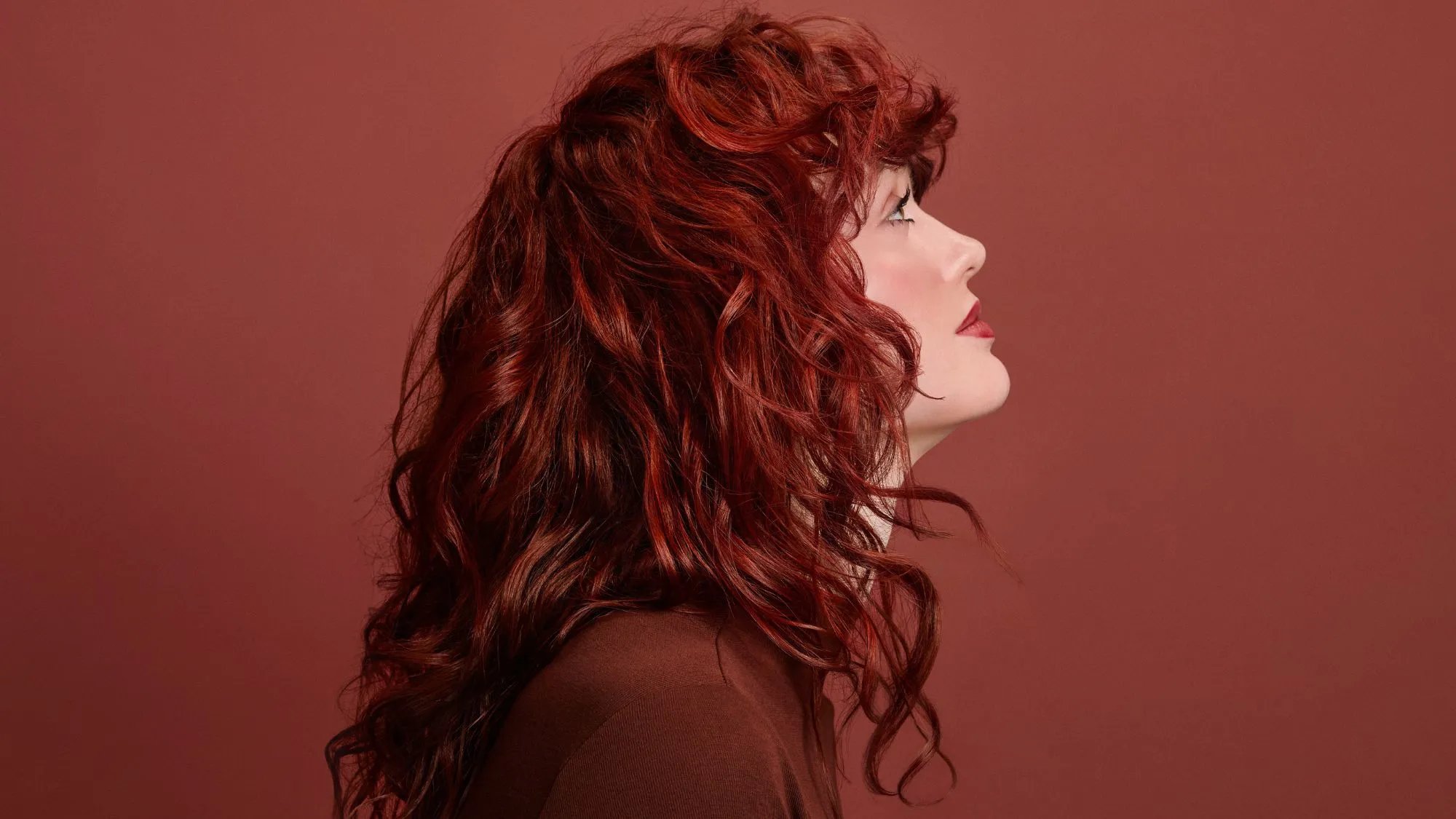Side profile of model with curly hair in a rich red wine shade.