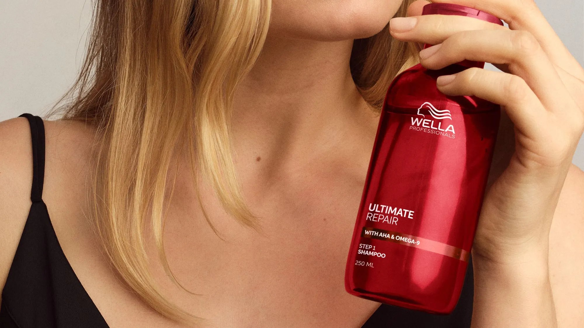 Model with blonde hair holds a bottle of ULTIMATE REPAIR Shampoo.
