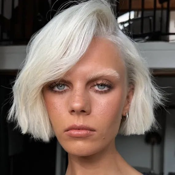 Model with white blonde micro bob swept to one side.