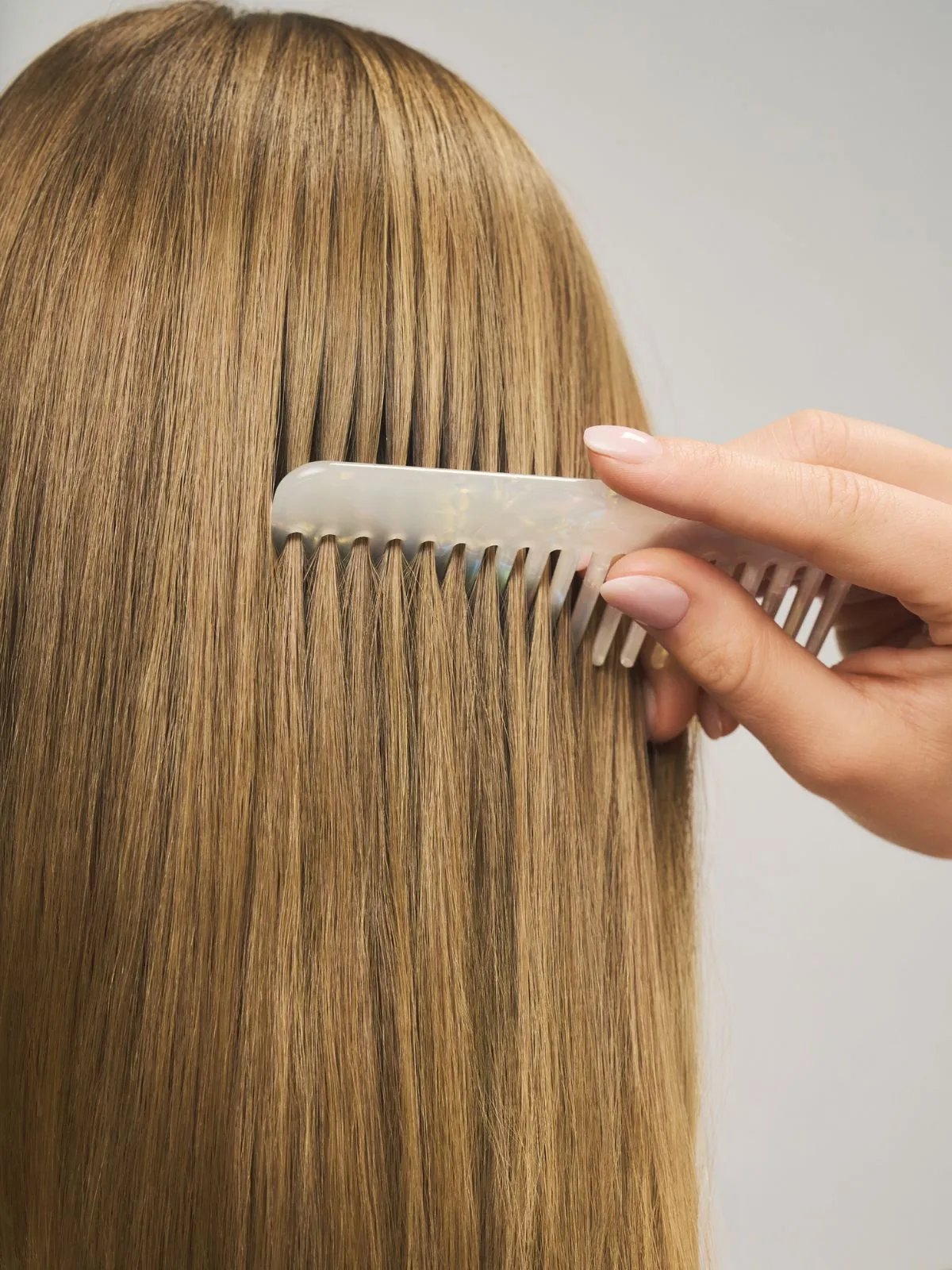 Model runs wide-tooth comb through golden blonde hair. 