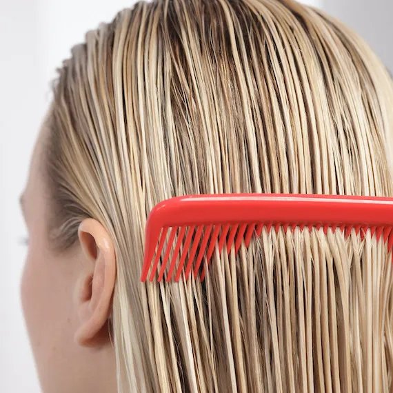 Le mannequin passe un peigne rouge sur ses cheveux mouillés.