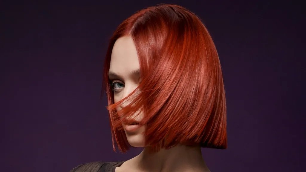 Model with mahogany red bob hair cut against a purple background. 