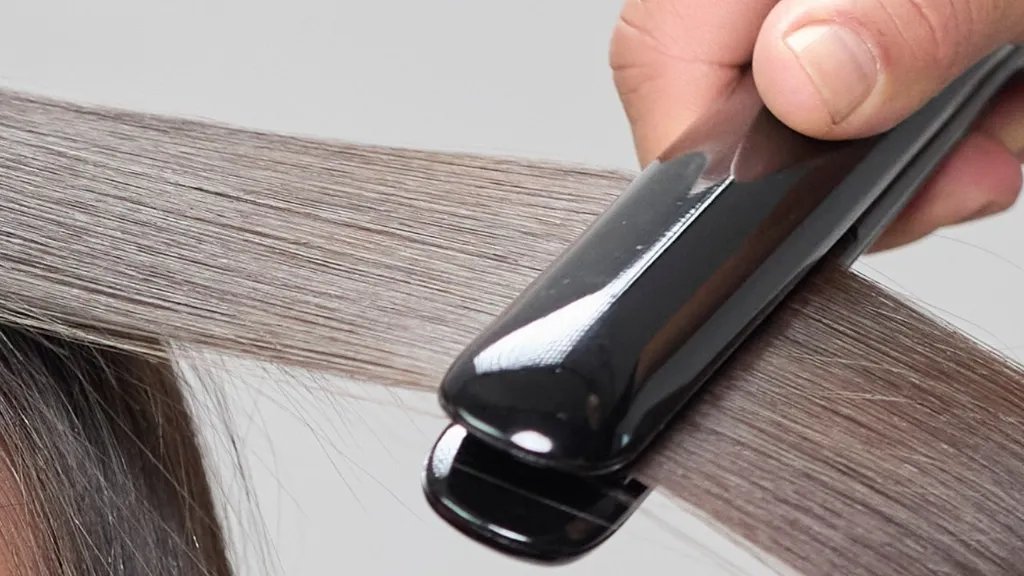 Close-up of hair being styled with a flat iron.