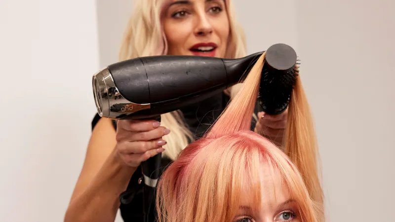 Model has their long, pink and blonde hair blow-dried by a stylist.