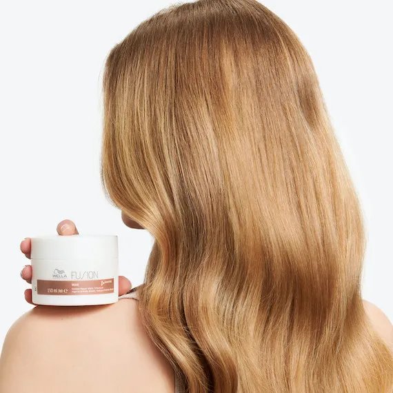 Model with long, glossy, blonde hair holds up Fusion Mask, which gives you up to 95% less breakage.