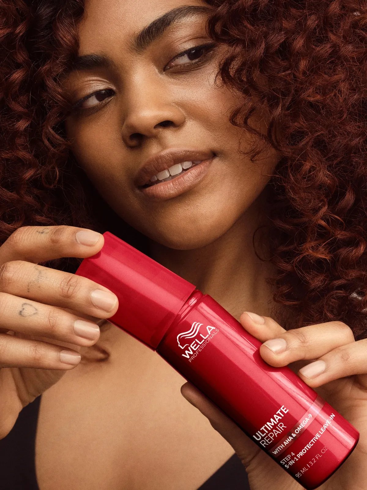 Model with dark, curly hair holds a bottle of ULTIMATE REPAIR Protective Leave-In.