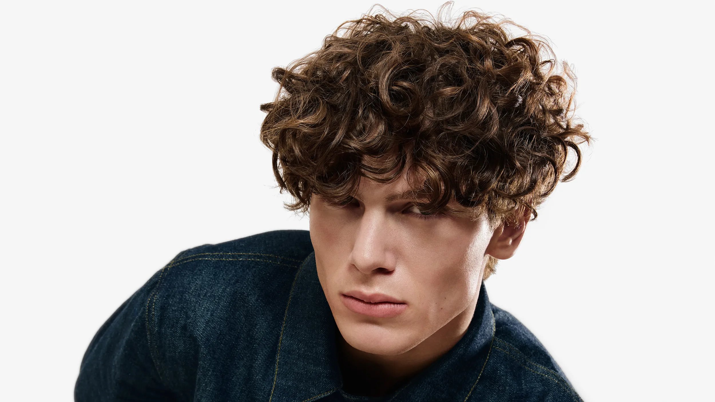 Portrait of a man with brown curly hair wearing a dark denim shirt against a white background.