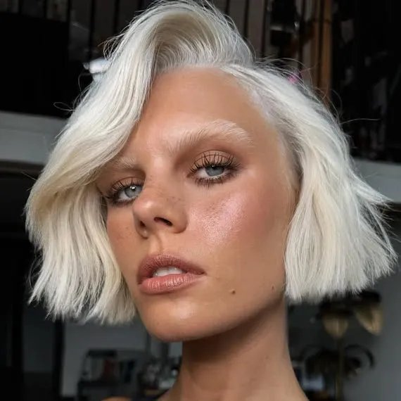 Model with white blonde micro bob swept to one side.