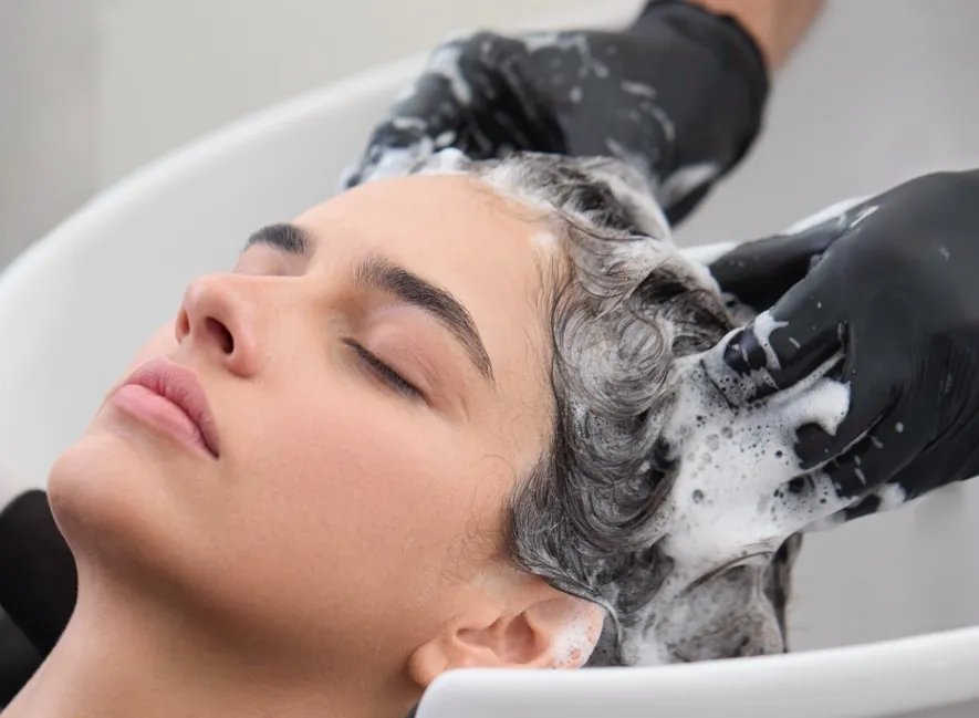 Hairstylist washes model’s hair at sink.