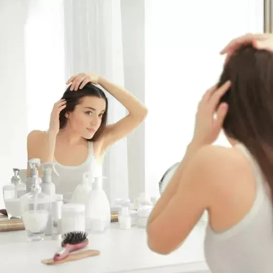 white brunette woman looking at her scalp in mirror reflection