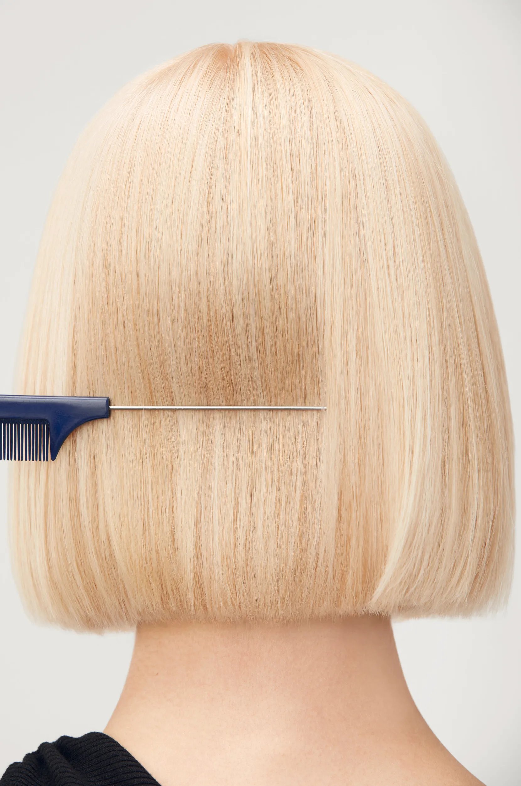 Back of woman’s head as her straight blonde hair is combed.