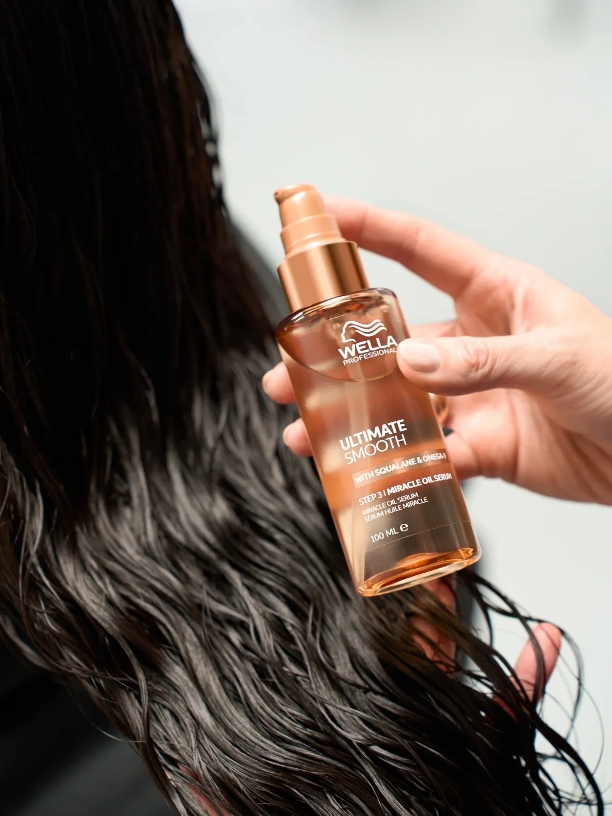 Il Miracle Oil Serum ULTIMATE SMOOTH tenuto accanto ai capelli scuri della modella.