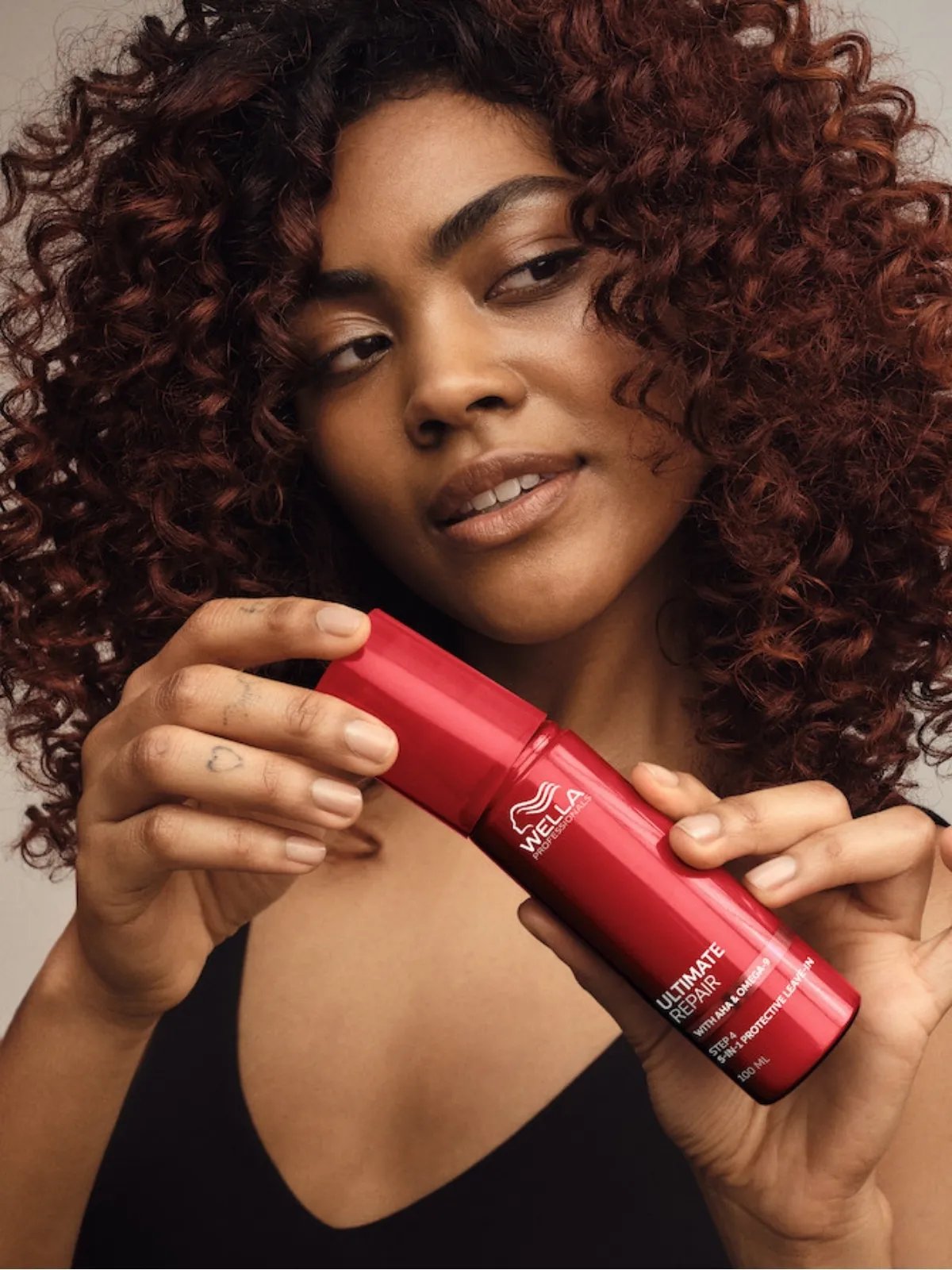 Model with dark, curly hair holds a bottle of ULTIMATE REPAIR Protective Leave-In.