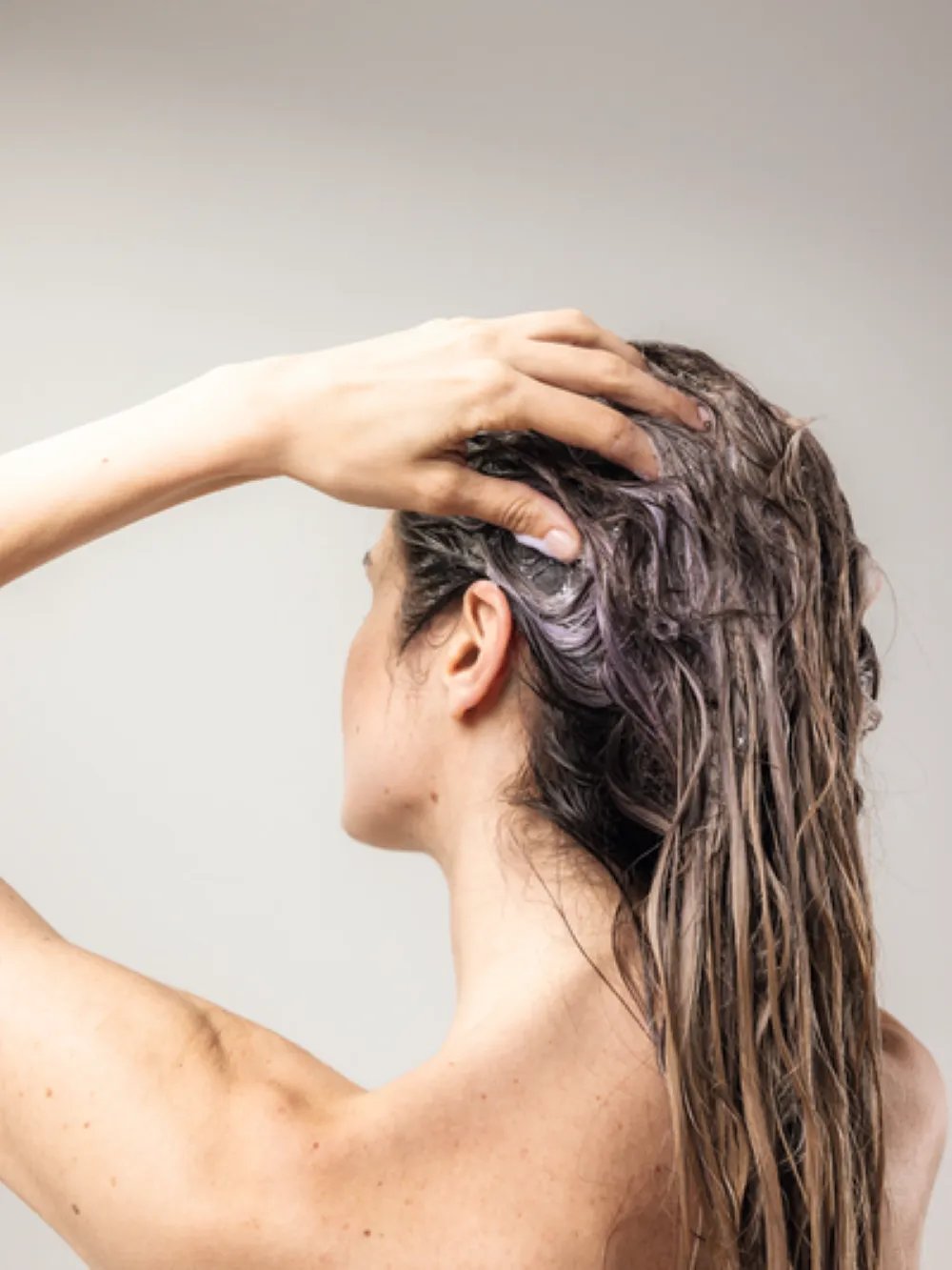 Model washing wet hair with shampoo lather during a hair care routine, created using Wella Professionals.